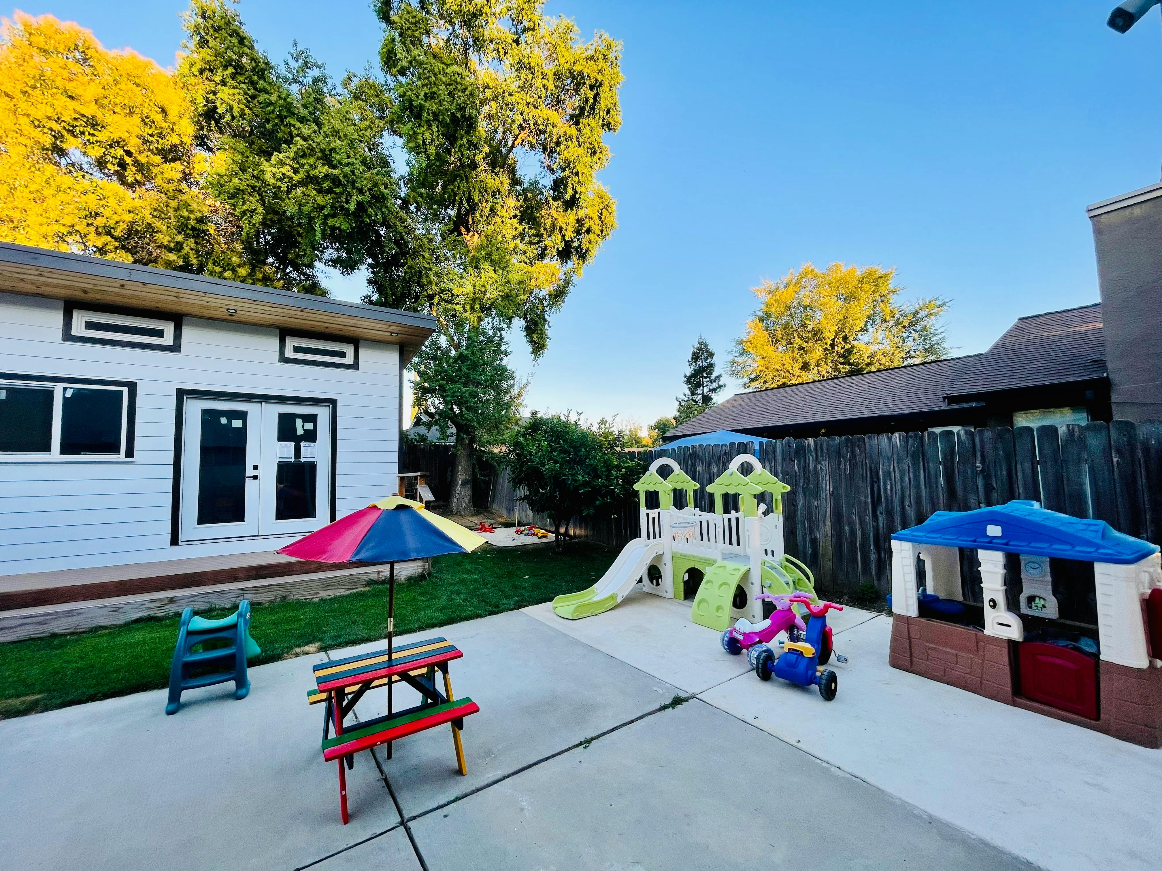 Outdoor play area with a small house, picnic table, and playground equipment
