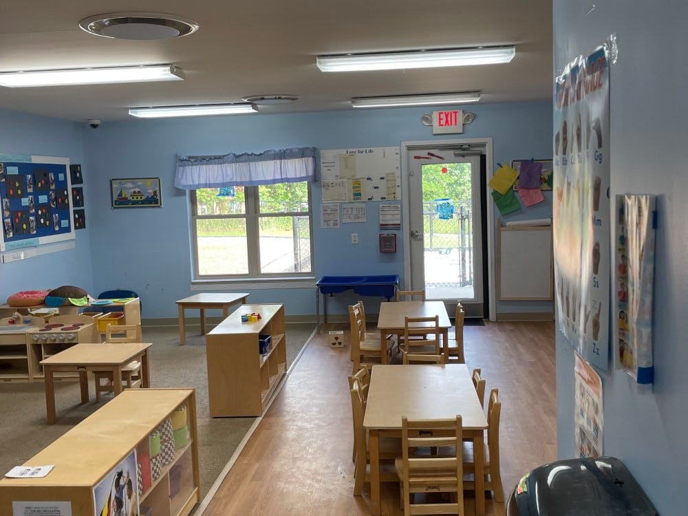 Empty classroom with small tables and chairs, toys, and an exit door