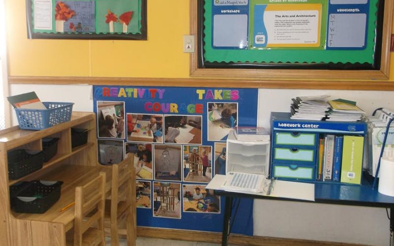Classroom corner with a wooden desk and chair, a bulletin board, and a homework center