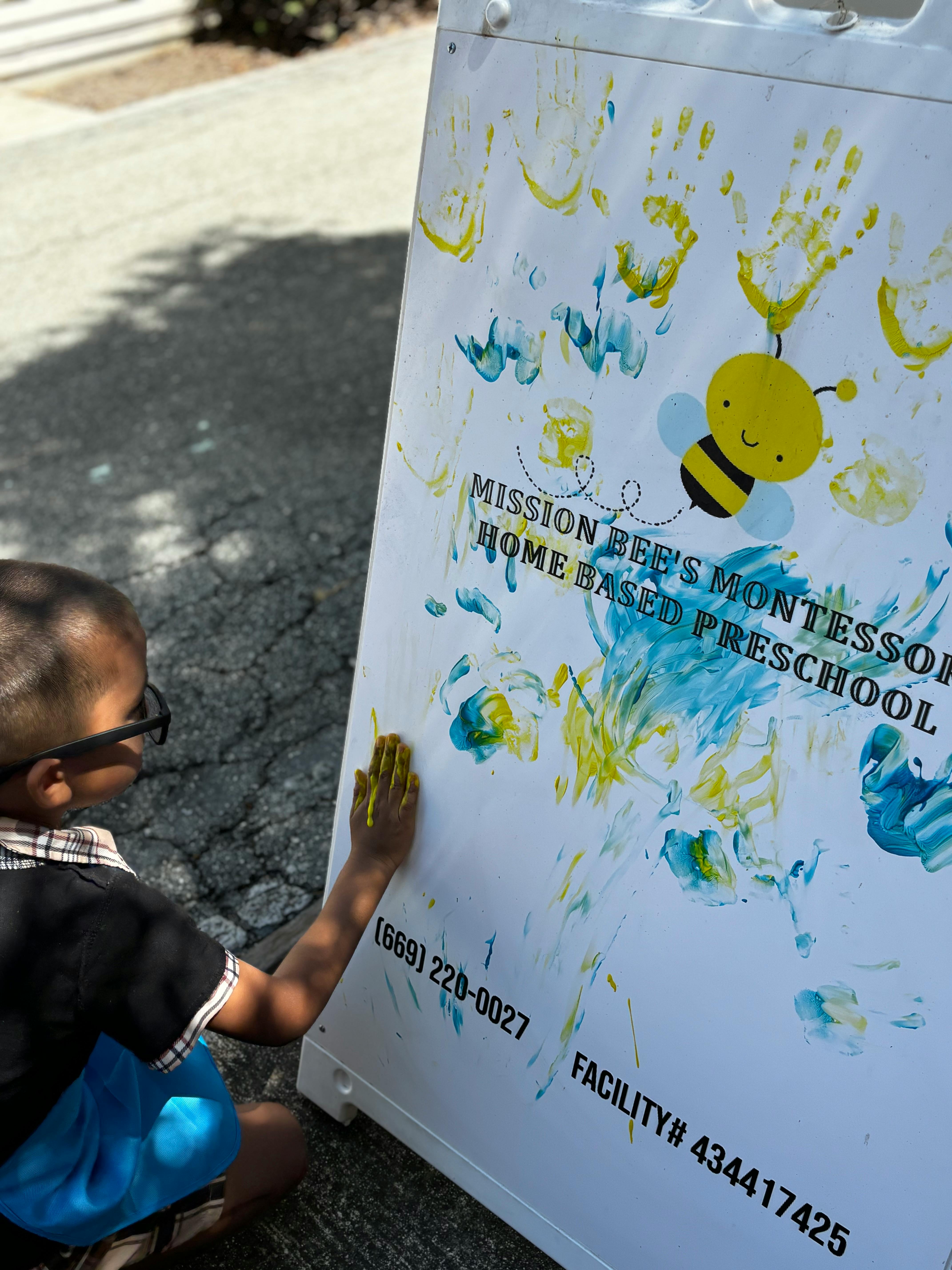 Child with paint on hand touching a sign with handprints and a bee graphic