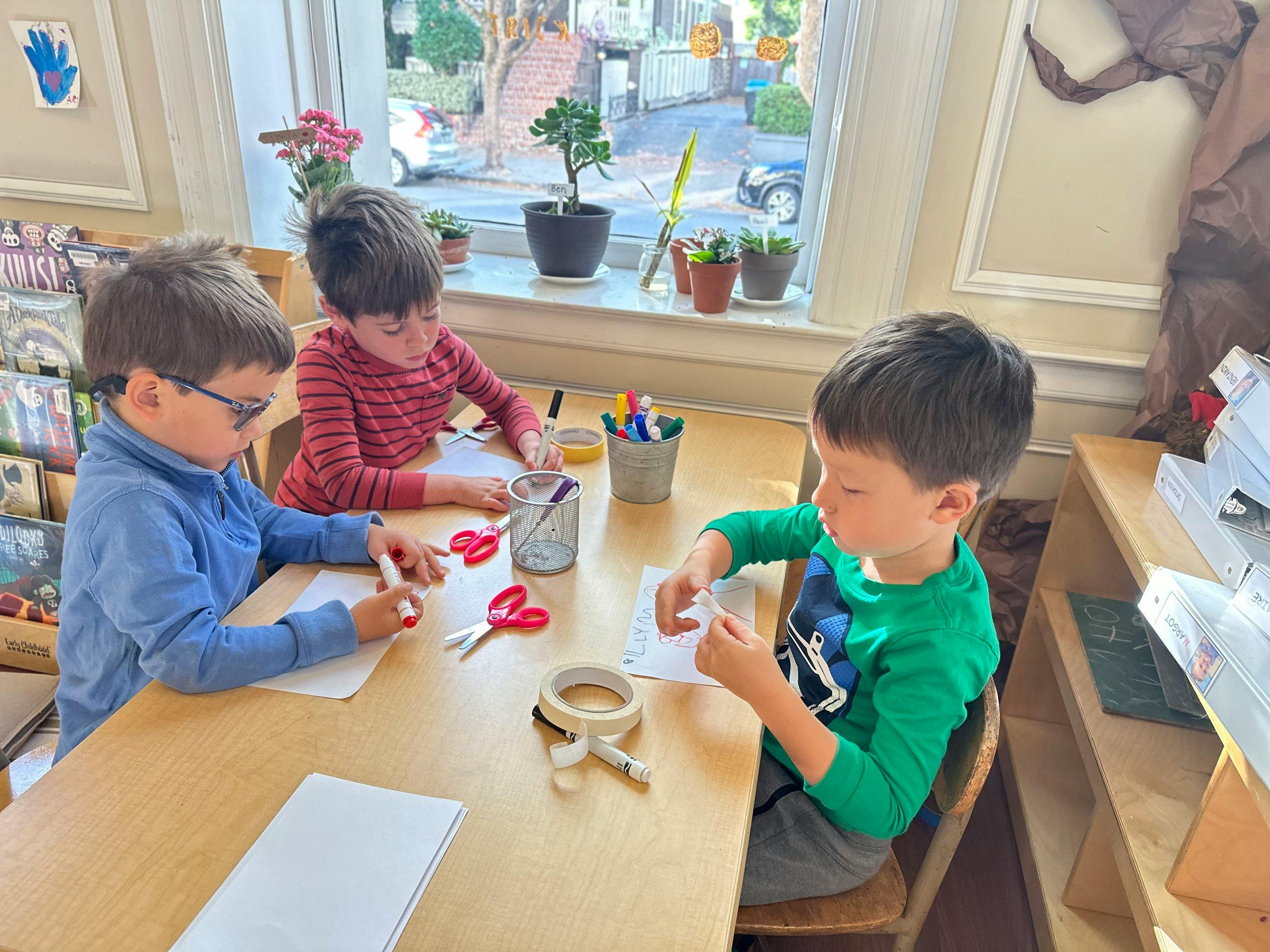 Three children sitting at a table doing crafts with paper and scissors