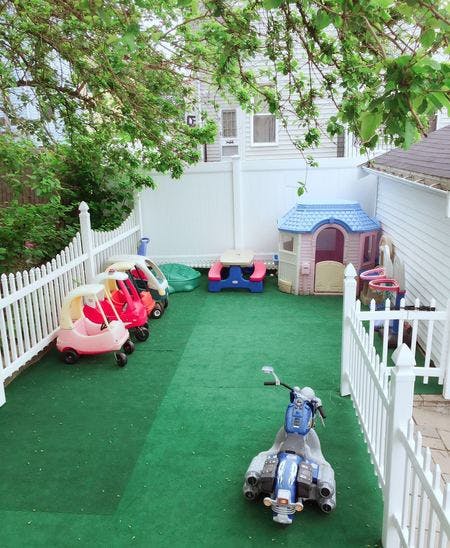 Outdoor play area with toy cars, playhouse, and scooter on green turf