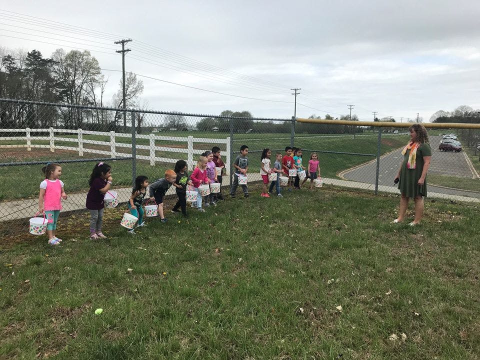Children with buckets lined up on grass with an adult nearby