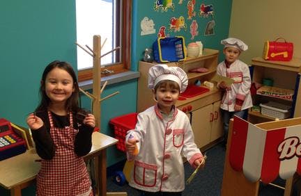Three children playing dress-up in a classroom
