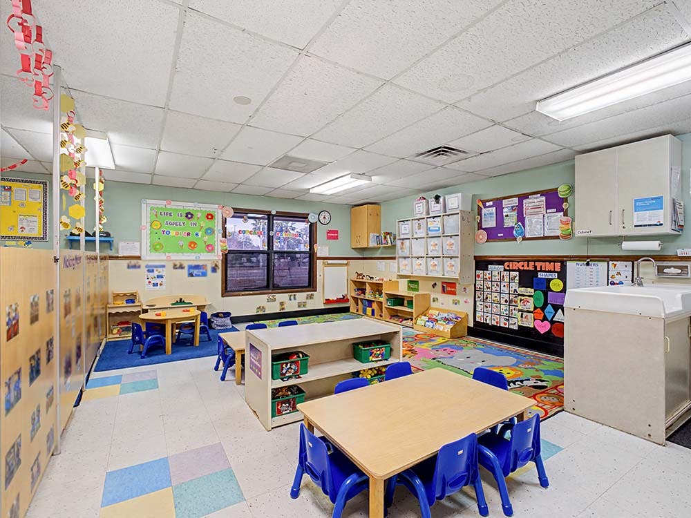 Empty colorful preschool classroom with tables, chairs, and learning materials