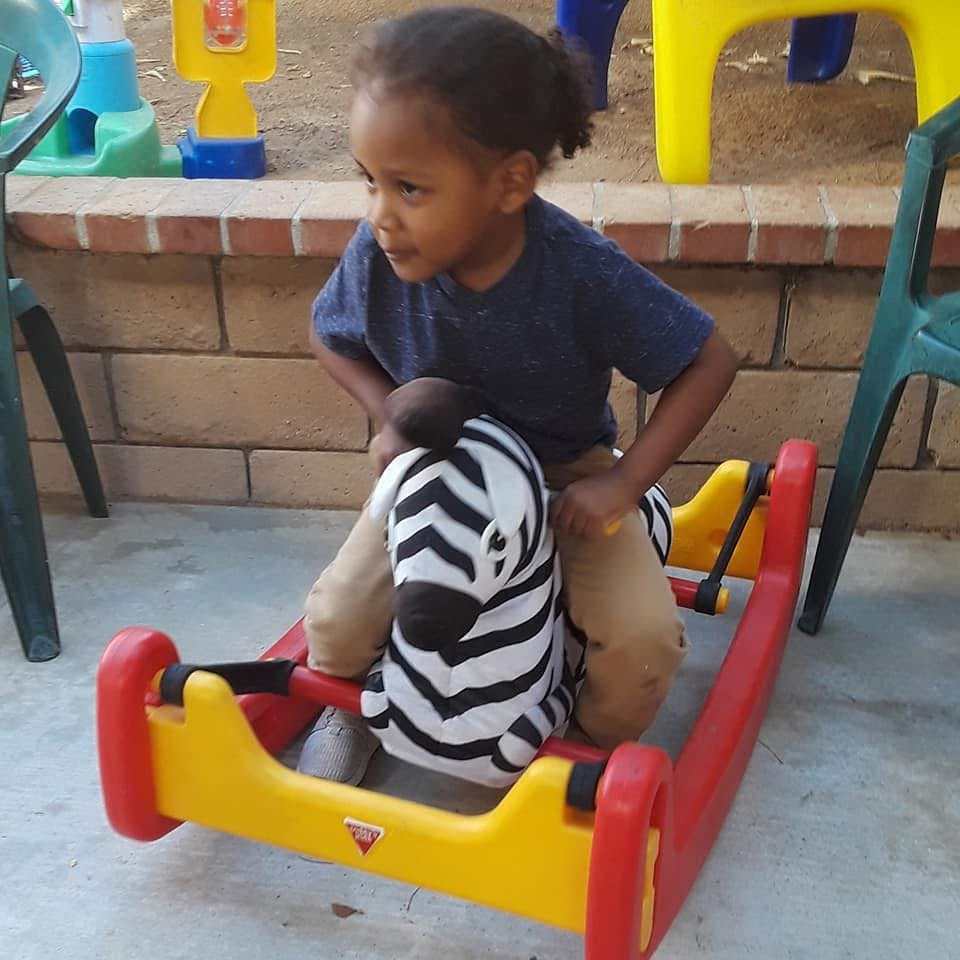Child riding a rocking zebra toy outdoors