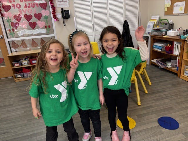 Three children in green shirts posing in a classroom
