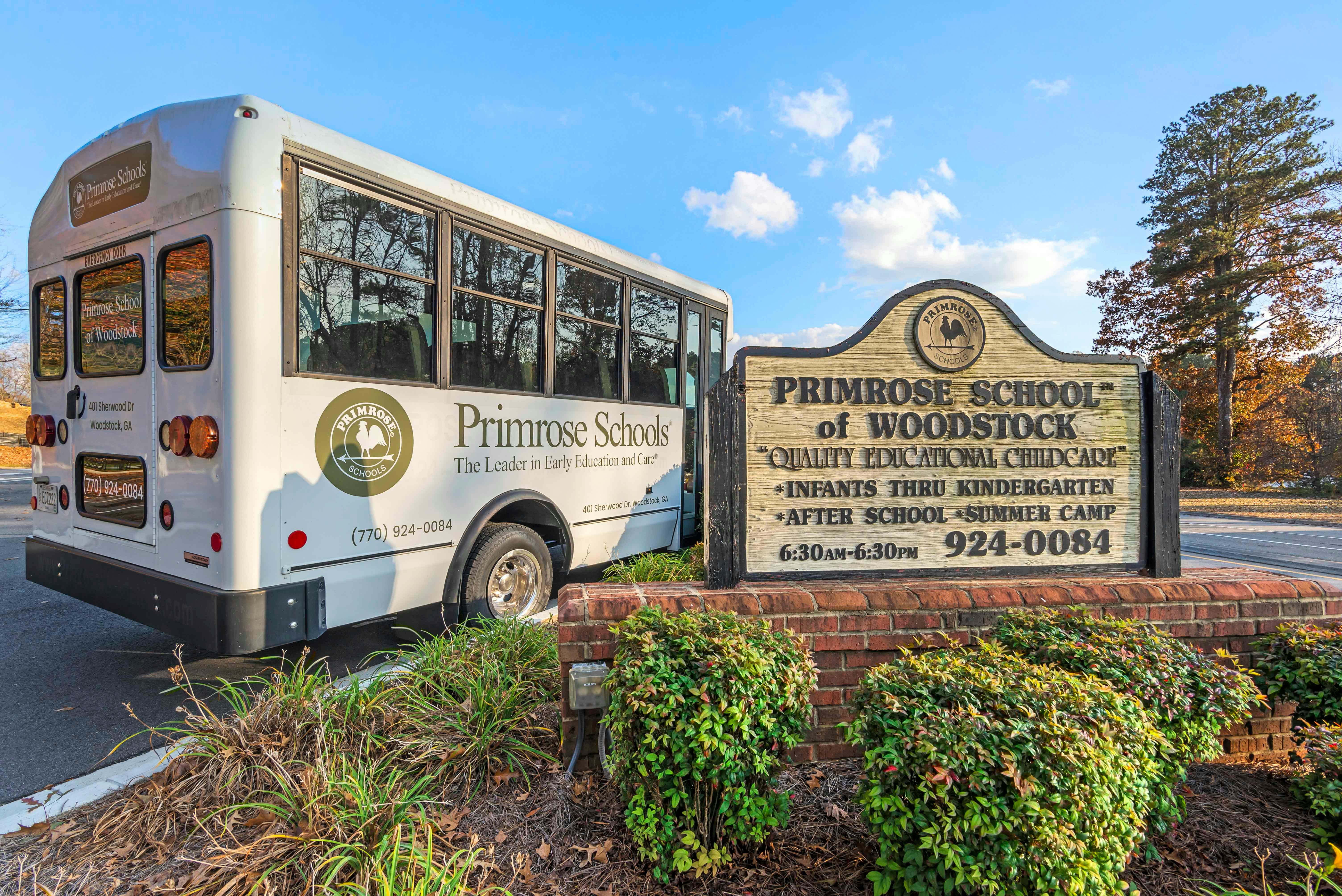 white Primrose Schools bus next to a wooden sign for Primrose School of Woodstock