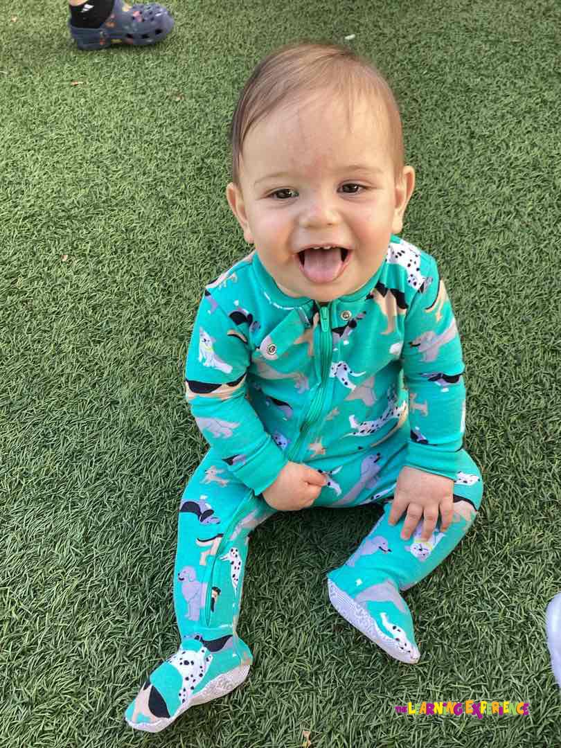 Child in a teal dog-patterned sleeper sitting on grass