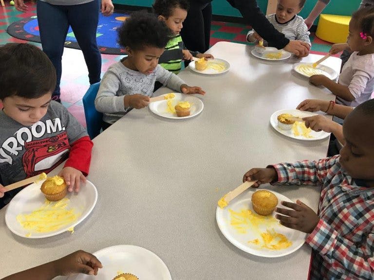 Children at a table decorating cupcakes with yellow frosting