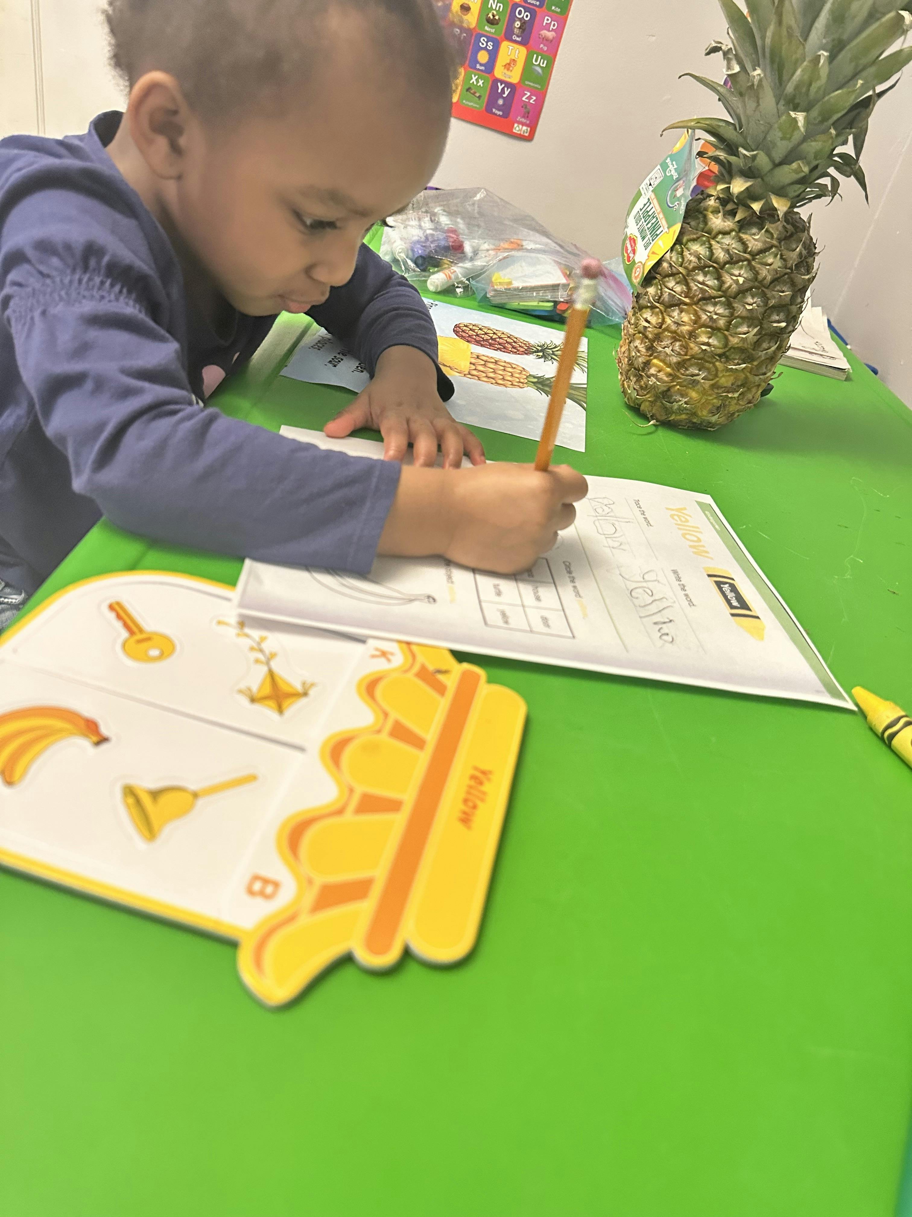 Child writing on a worksheet at a table with a pineapple