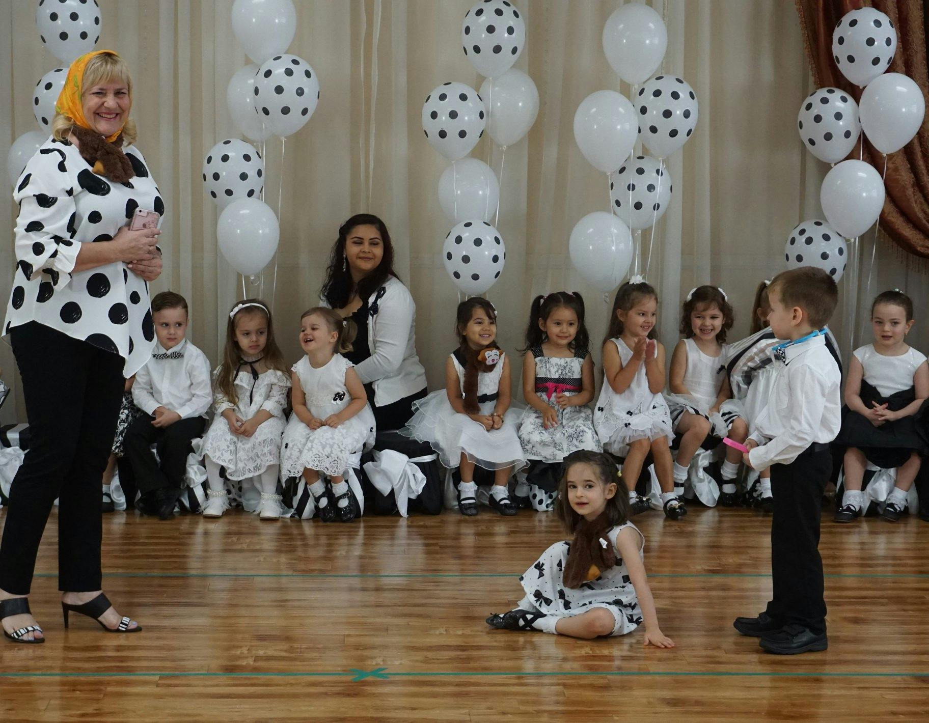 Adults and children in white and black polka dot outfits with balloons