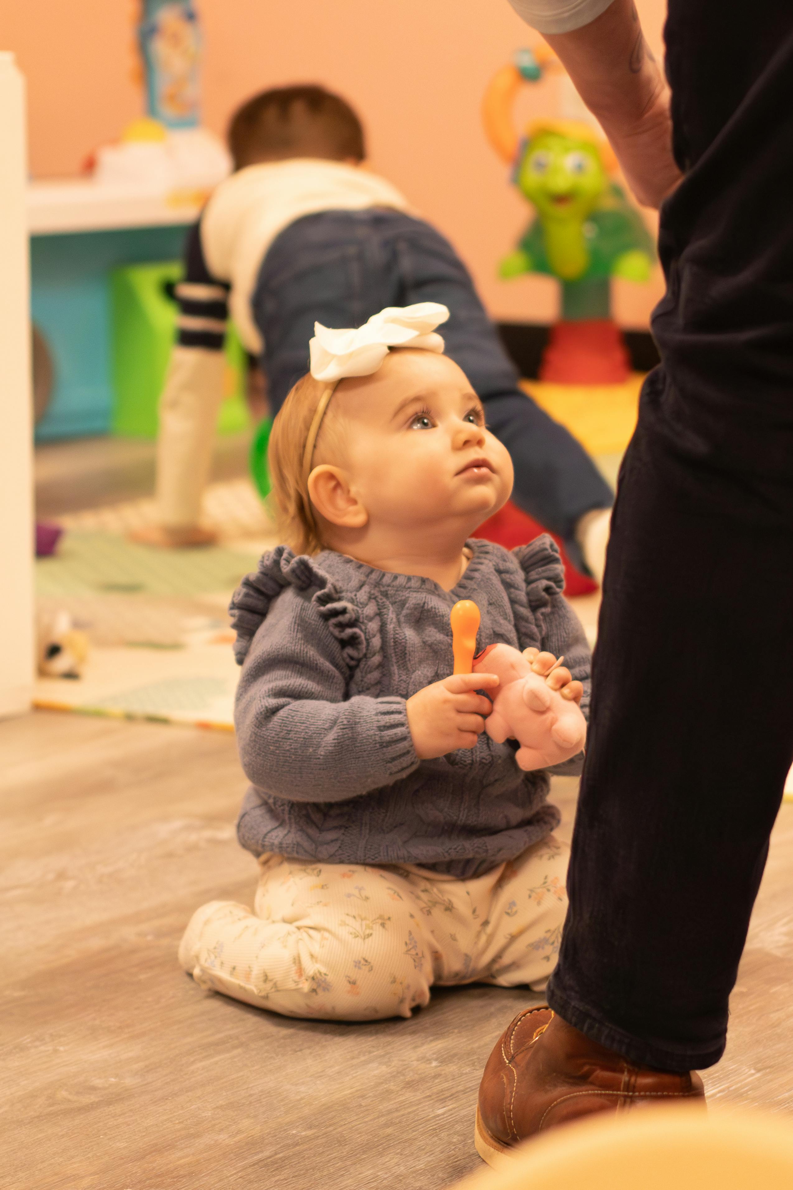 Child kneeling on floor holding a toy, looking up at a person