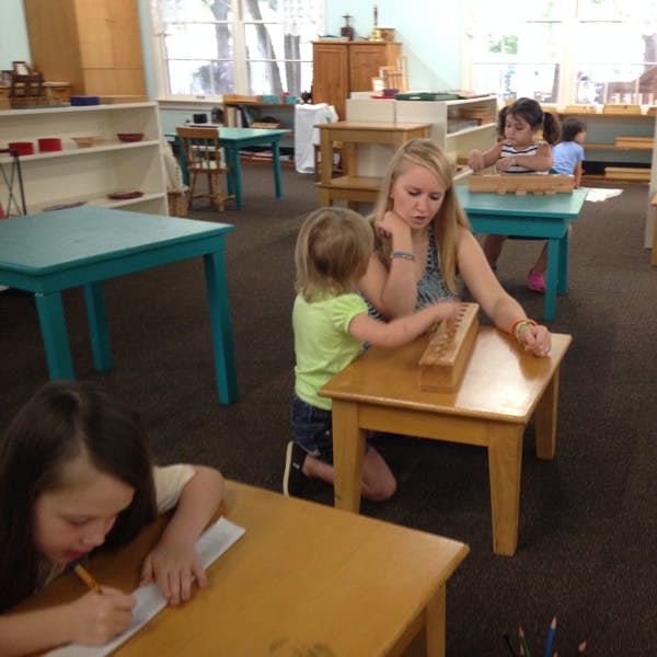 Adult and child interacting with a wooden learning toy in a classroom
