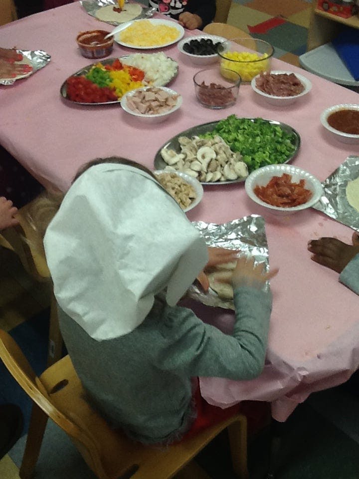 Child wearing a paper chef hat making food at a table with many ingredients