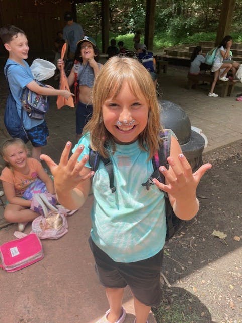 Child with white substance on nose and painted fingernails holding up hands