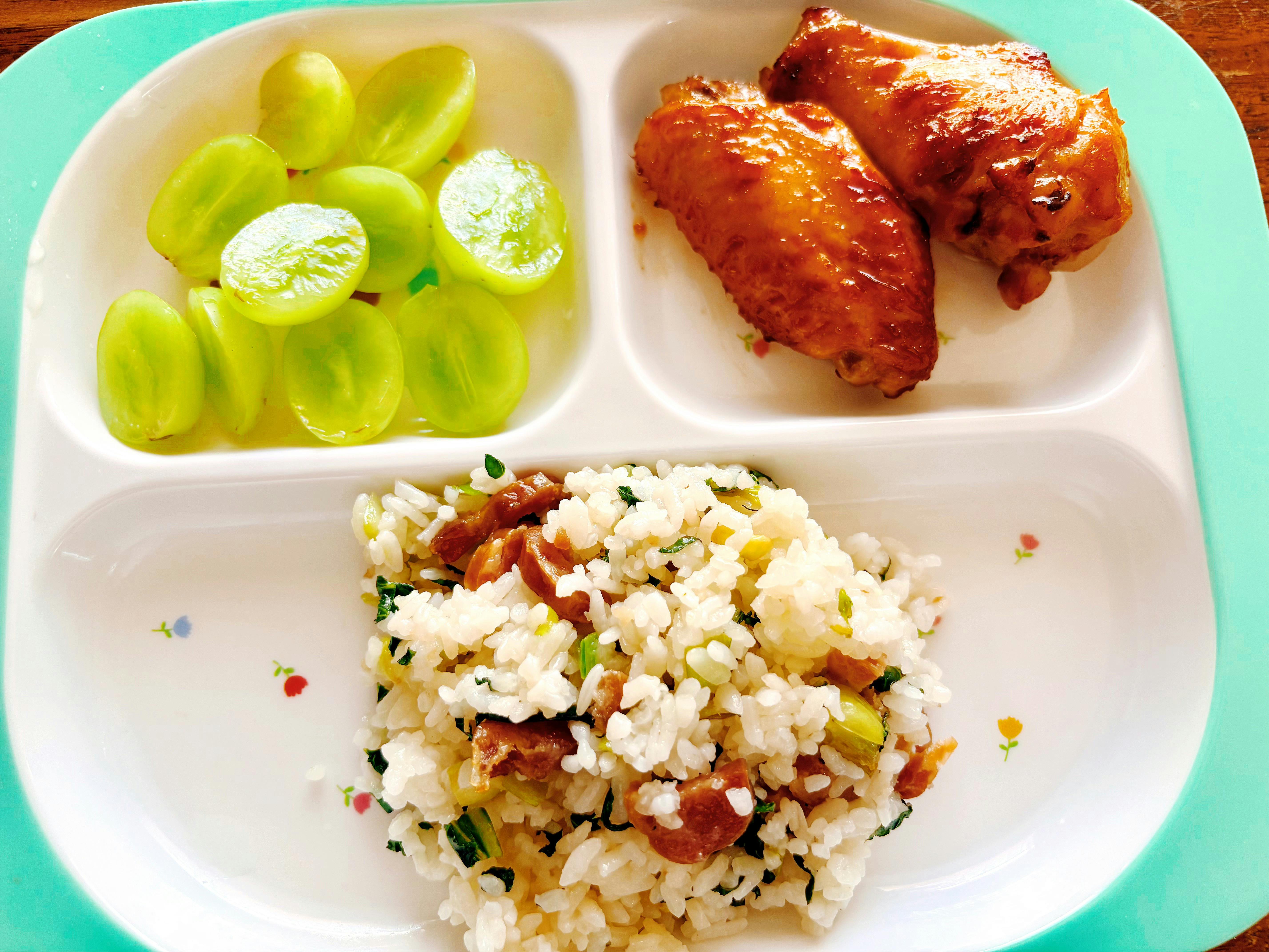 Divided tray with sliced grapes, chicken wings, and fried rice