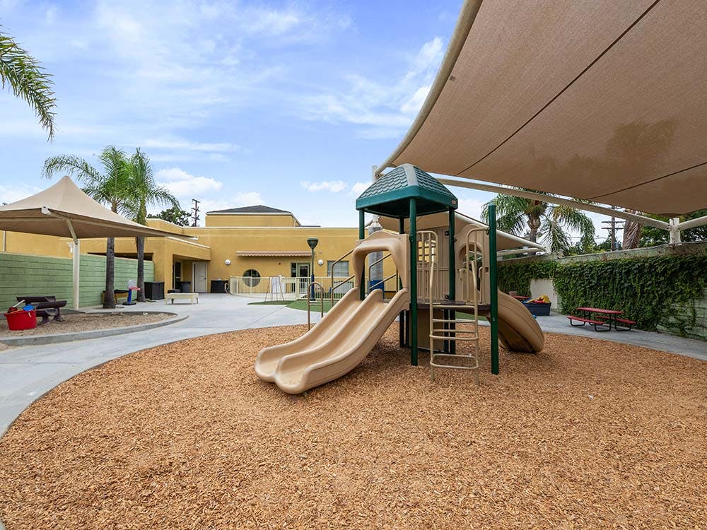 Outdoor playground with slides, play structures, and shaded areas