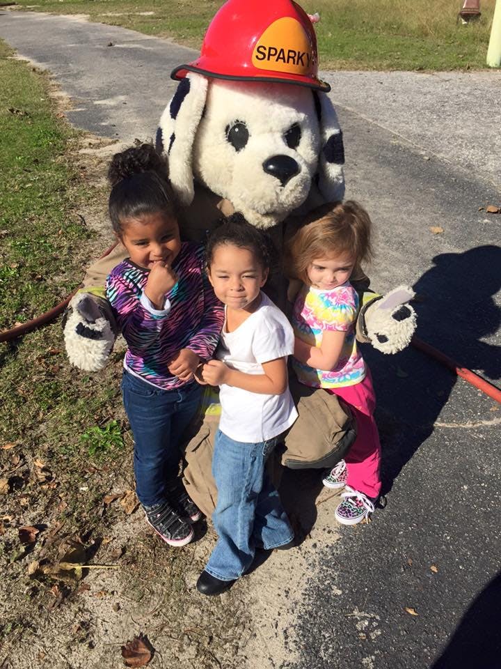 Three children with a person in a Sparky the Fire Dog costume