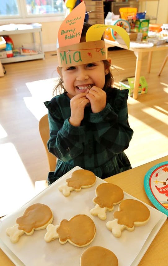 Child wearing a paper headband with "Mia" written on it, eating a cookie
