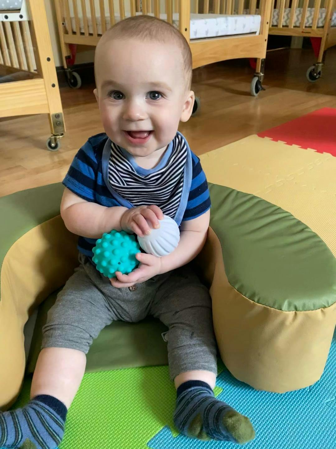 Child sitting in a soft chair holding two textured balls