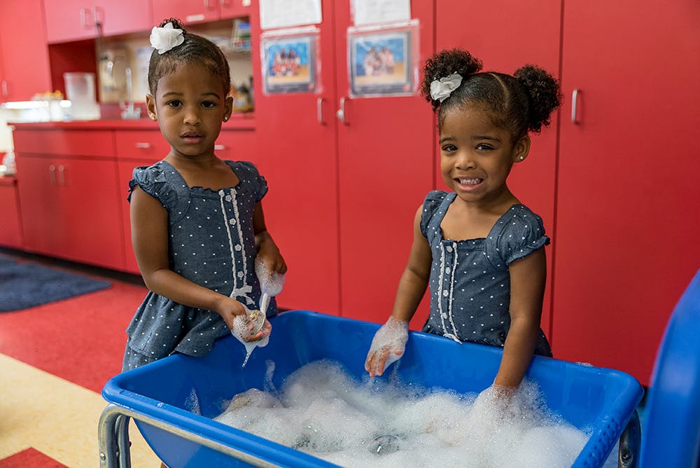 Two children playing with bubbles in a blue bin