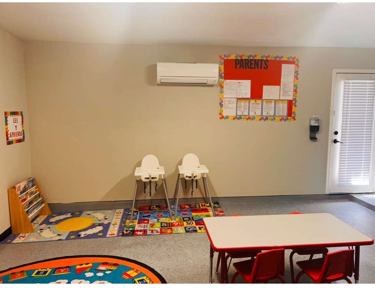 Childcare room with tables, chairs, high chairs, rugs, and a "Parents" bulletin board