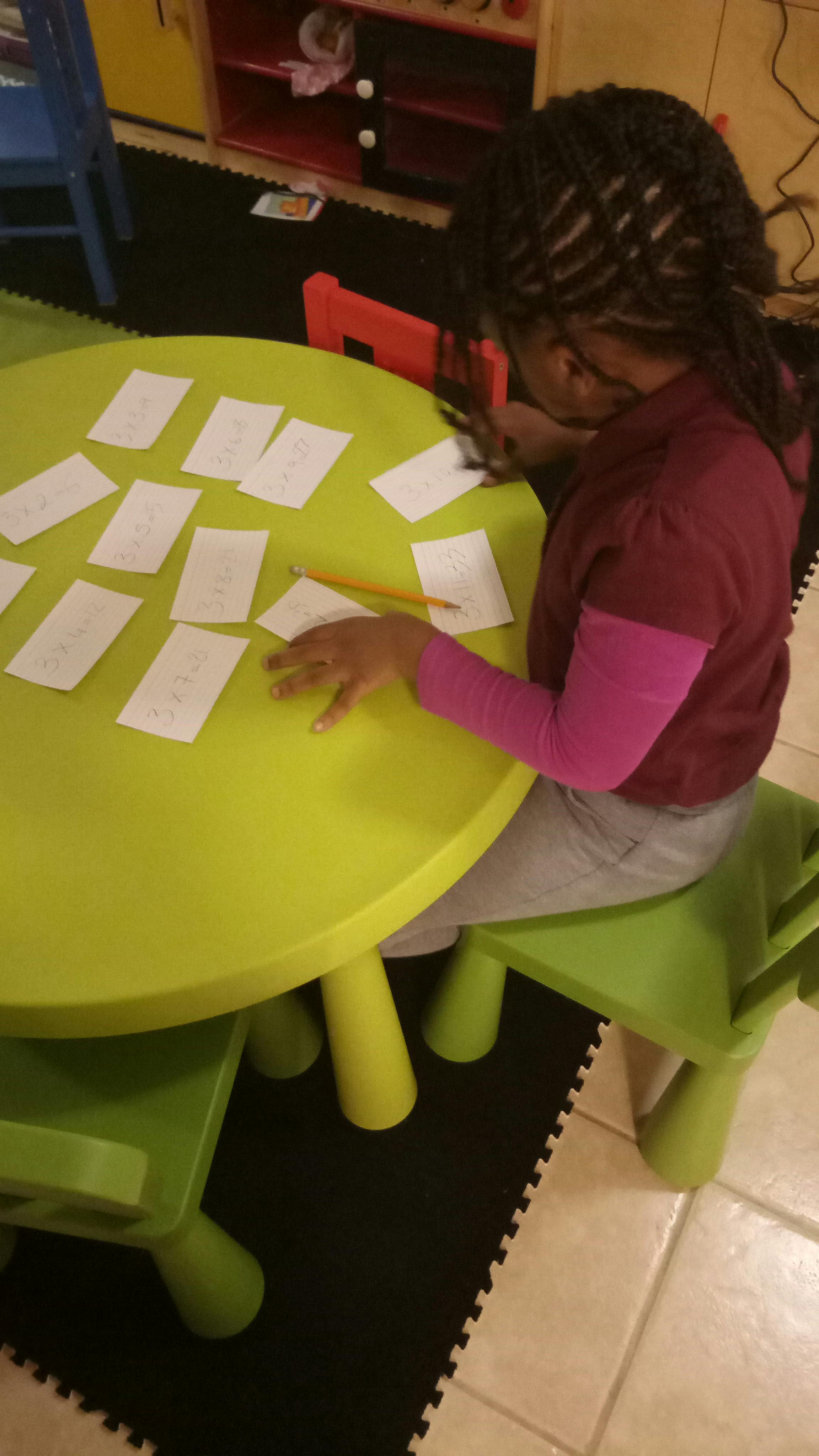 Child sitting at a table with cards and writing on small cards
