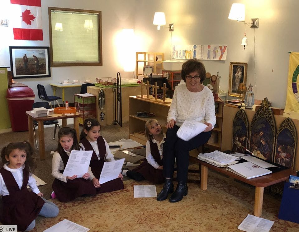 Adult and children in a classroom holding papers