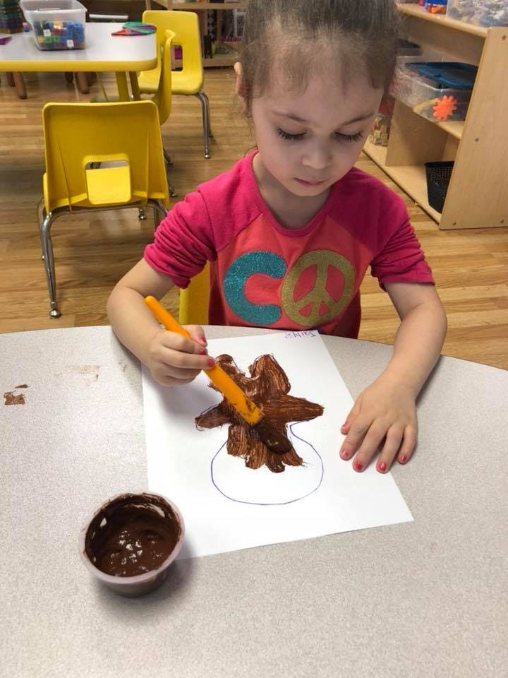 Child painting a tree on paper with a brush