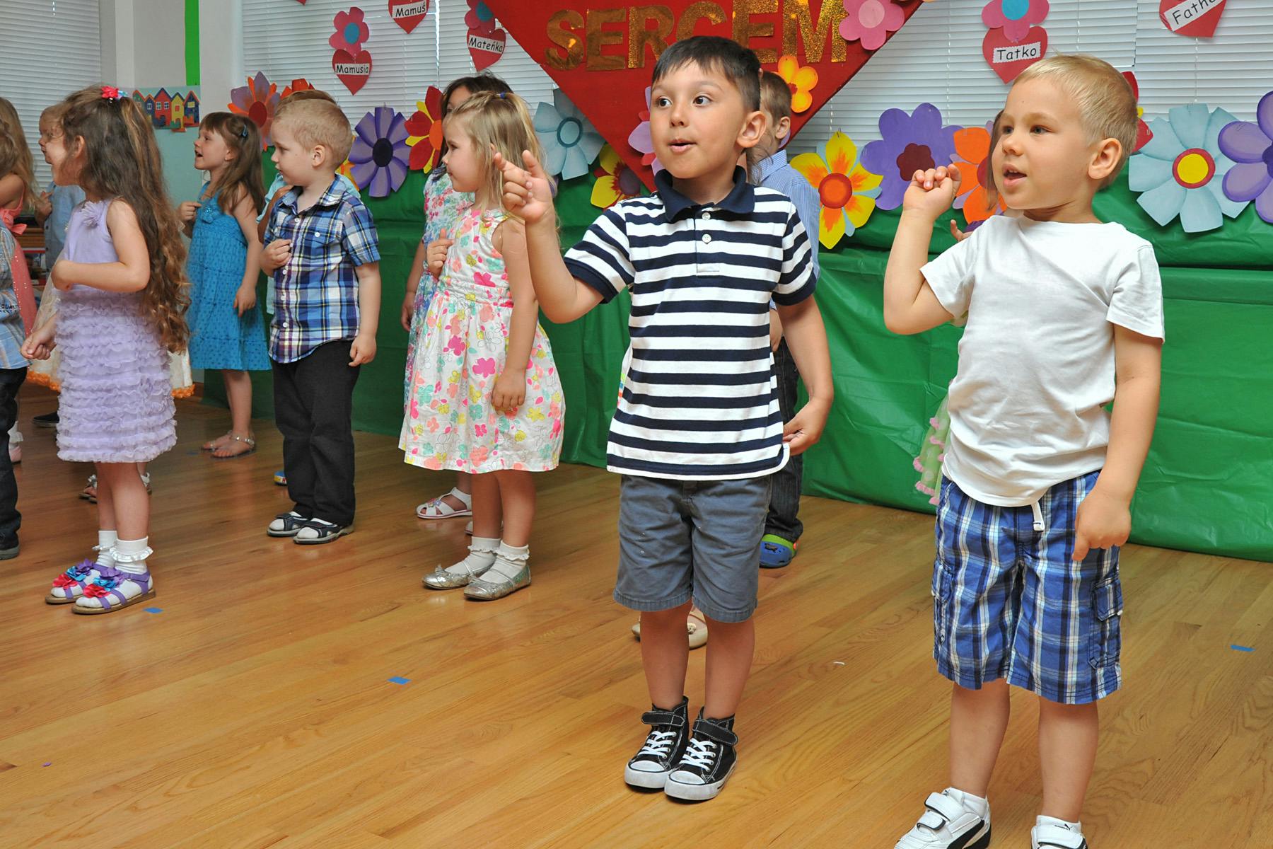 Children standing in a line, two boys in front raising their hands