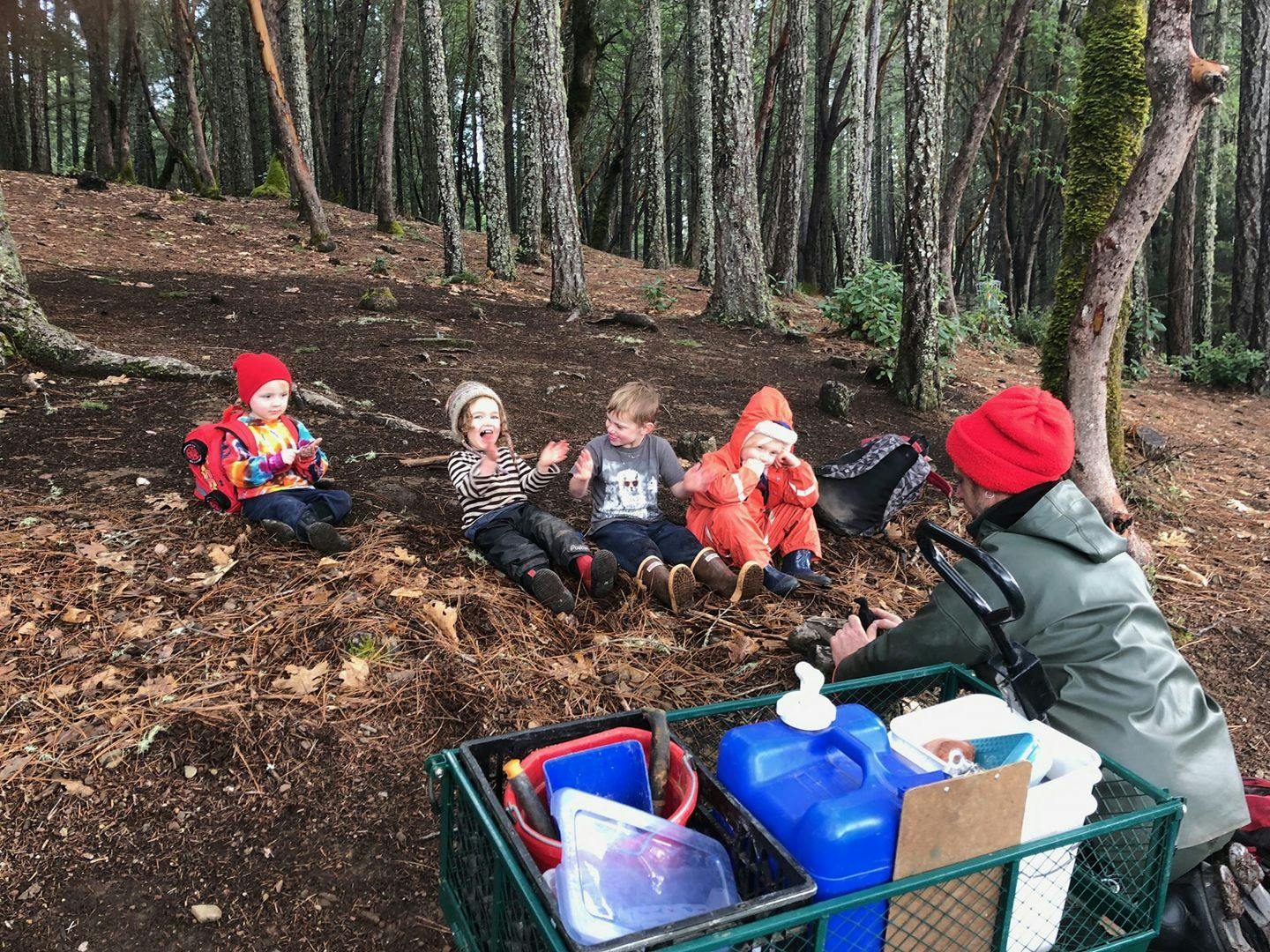 Children sitting on a forest floor with a person pushing a cart