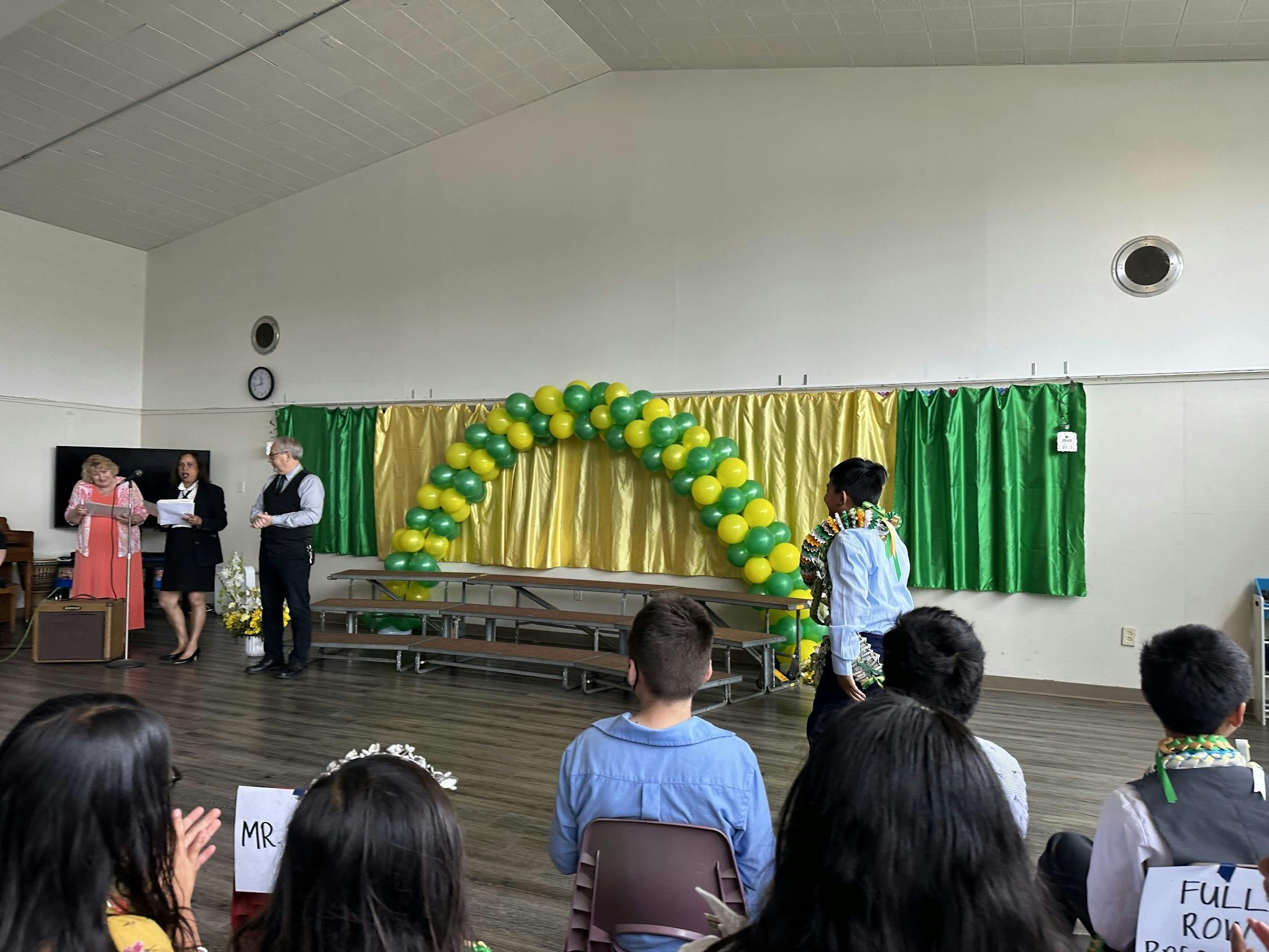 People on a stage with a balloon arch, facing an audience