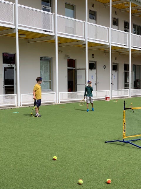 Two children holding tennis rackets on a green court
