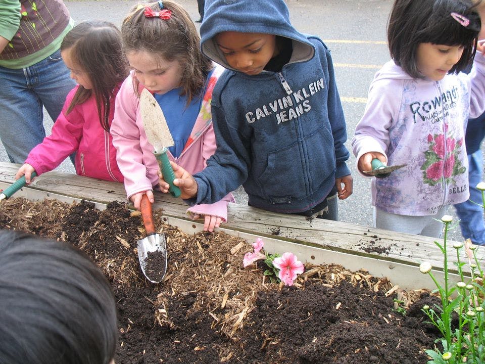 Children planting in a raised garden bed with small shovels