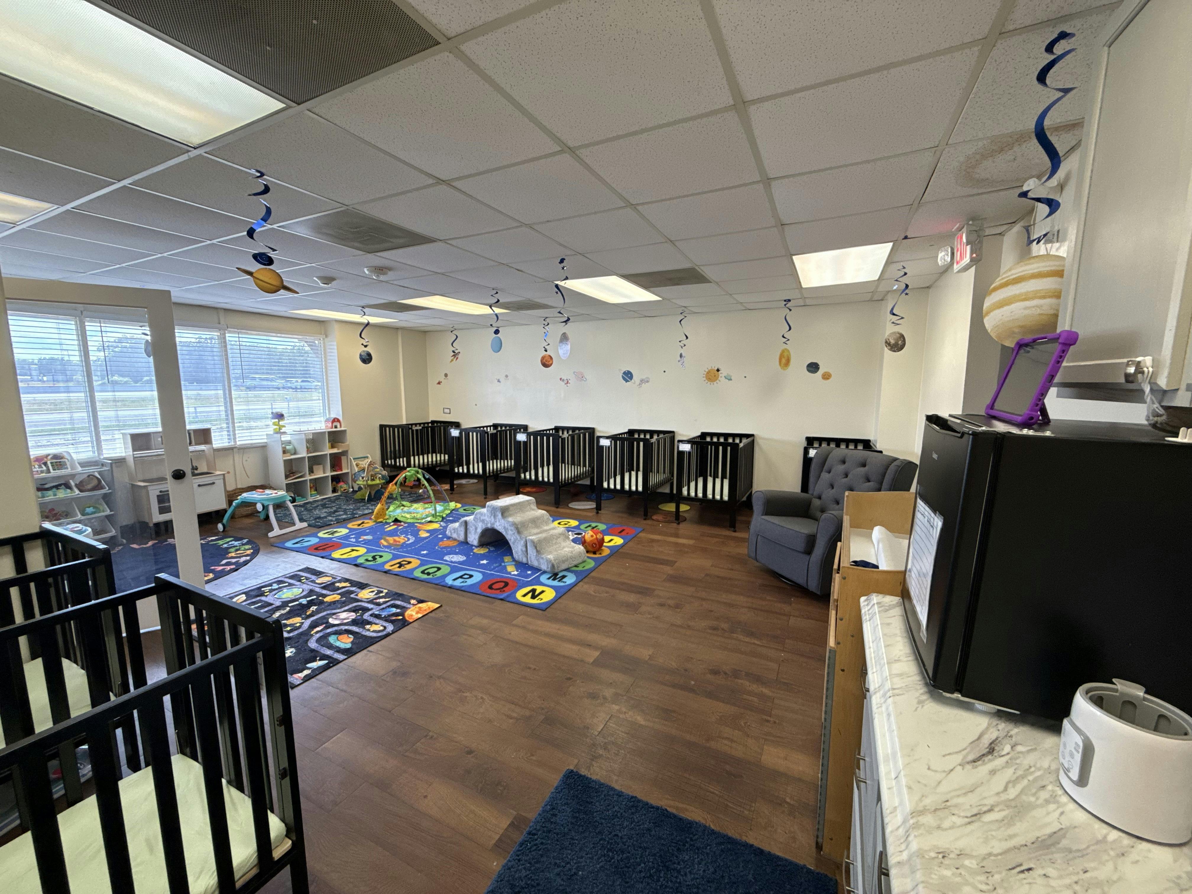 Cribs and play rugs in a brightly lit infant classroom