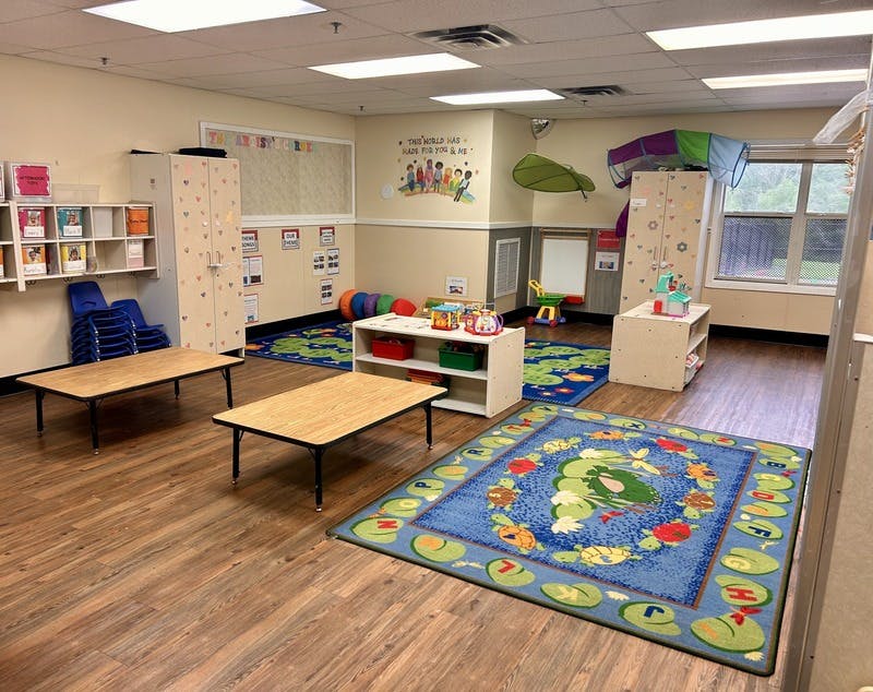 A classroom with small tables, colorful rugs, and play furniture