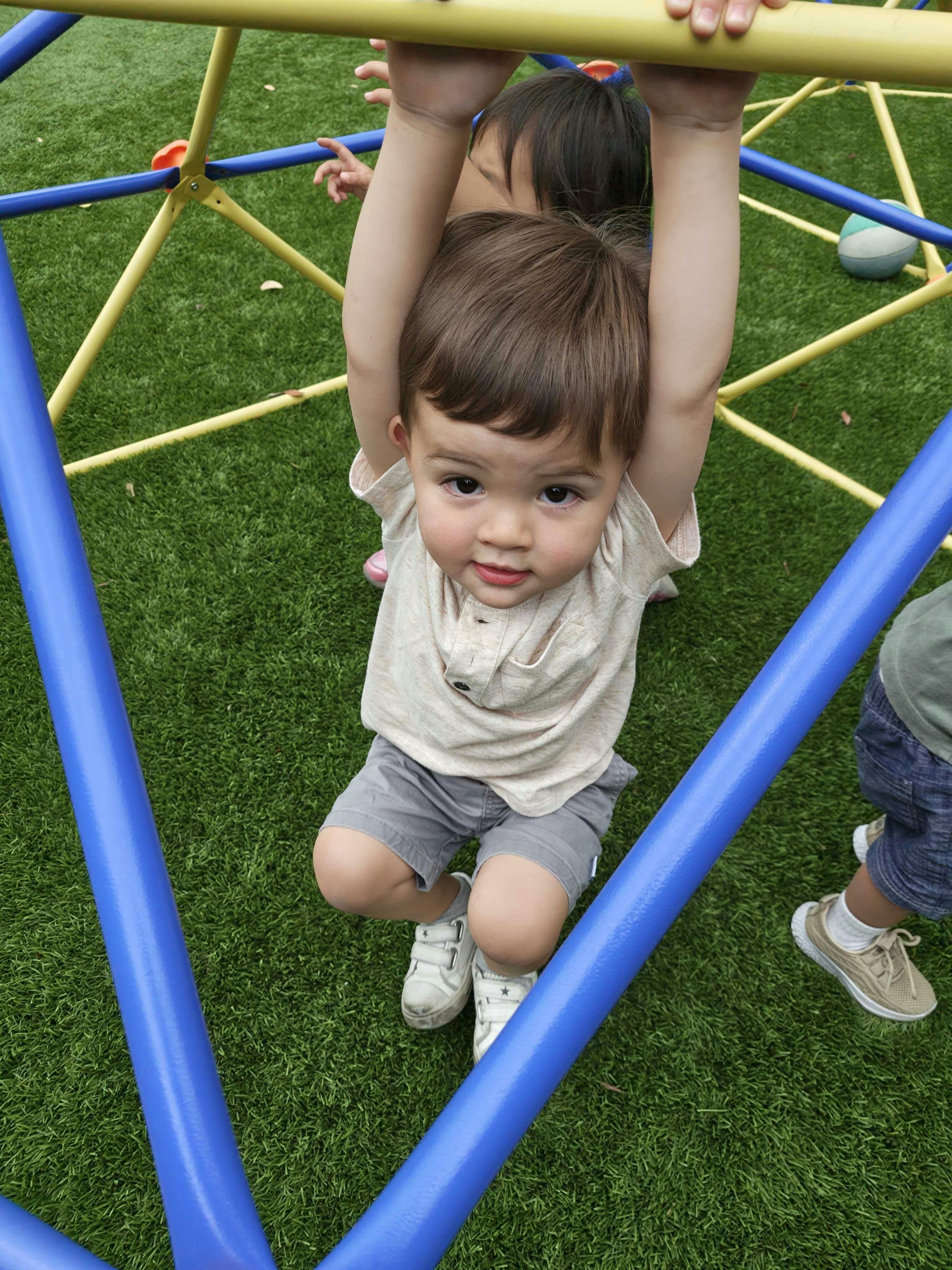 Child hanging from a jungle gym bar