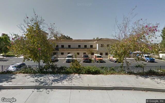 Building with a parking lot in front, trees and a fence
