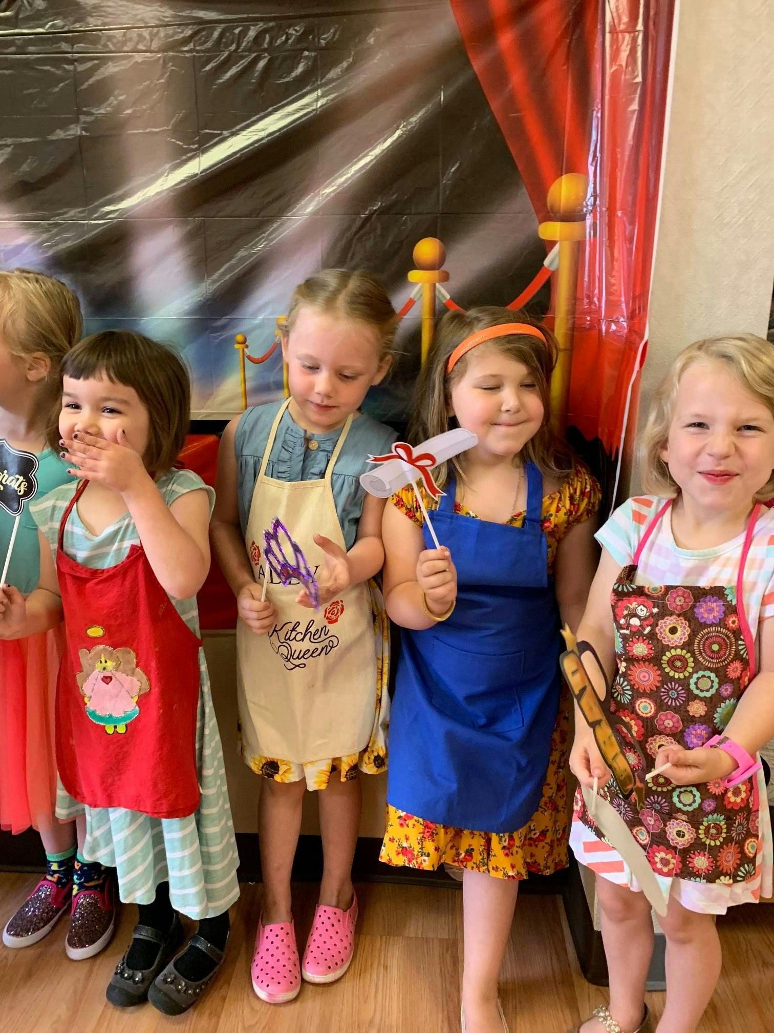Four children wearing aprons and holding craft sticks
