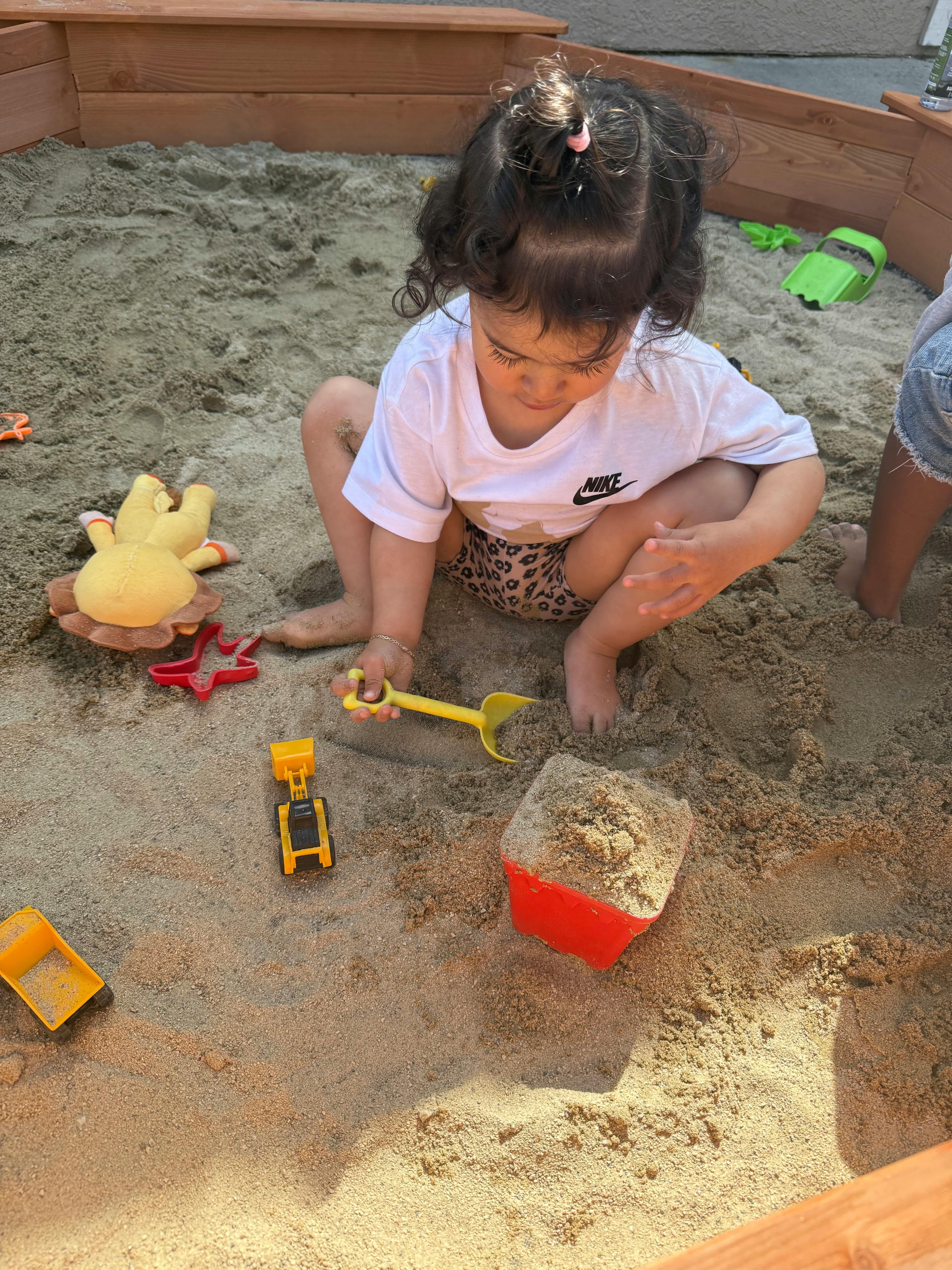 Child playing in a sandbox with a shovel and toys