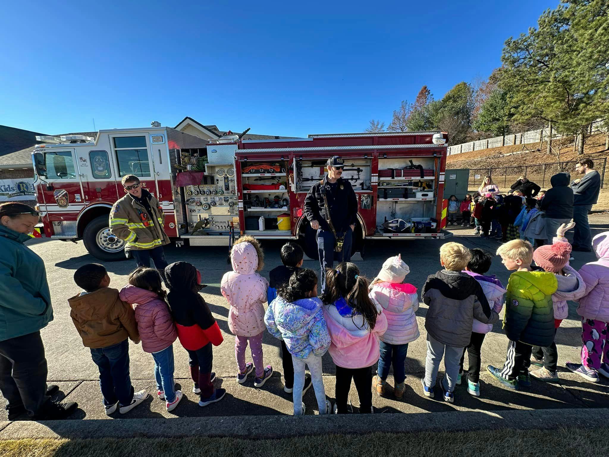 People and children gathered around a fire truck with firefighters