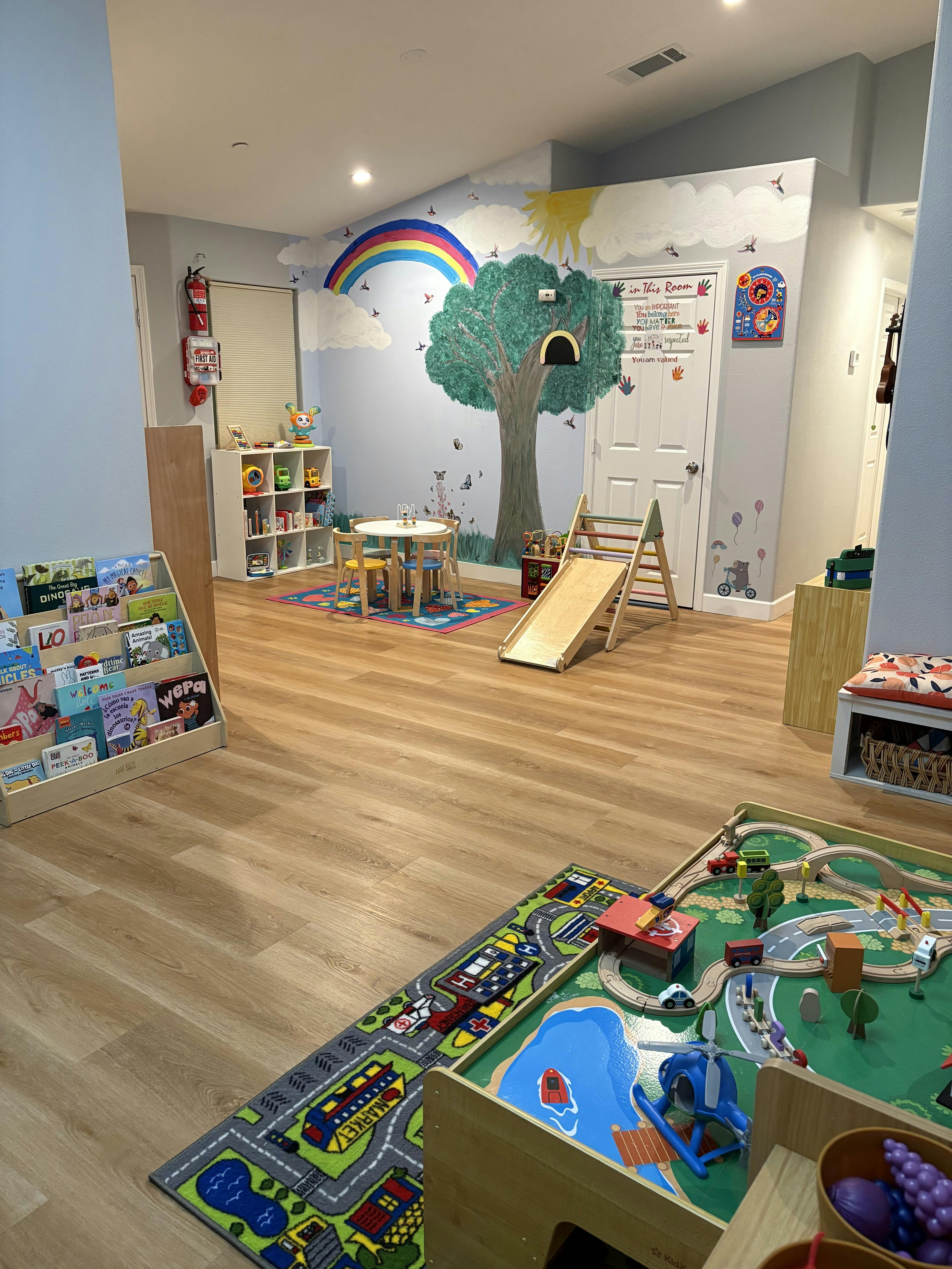 Playroom with a colorful wall mural, small table and chairs, a slide, and toys