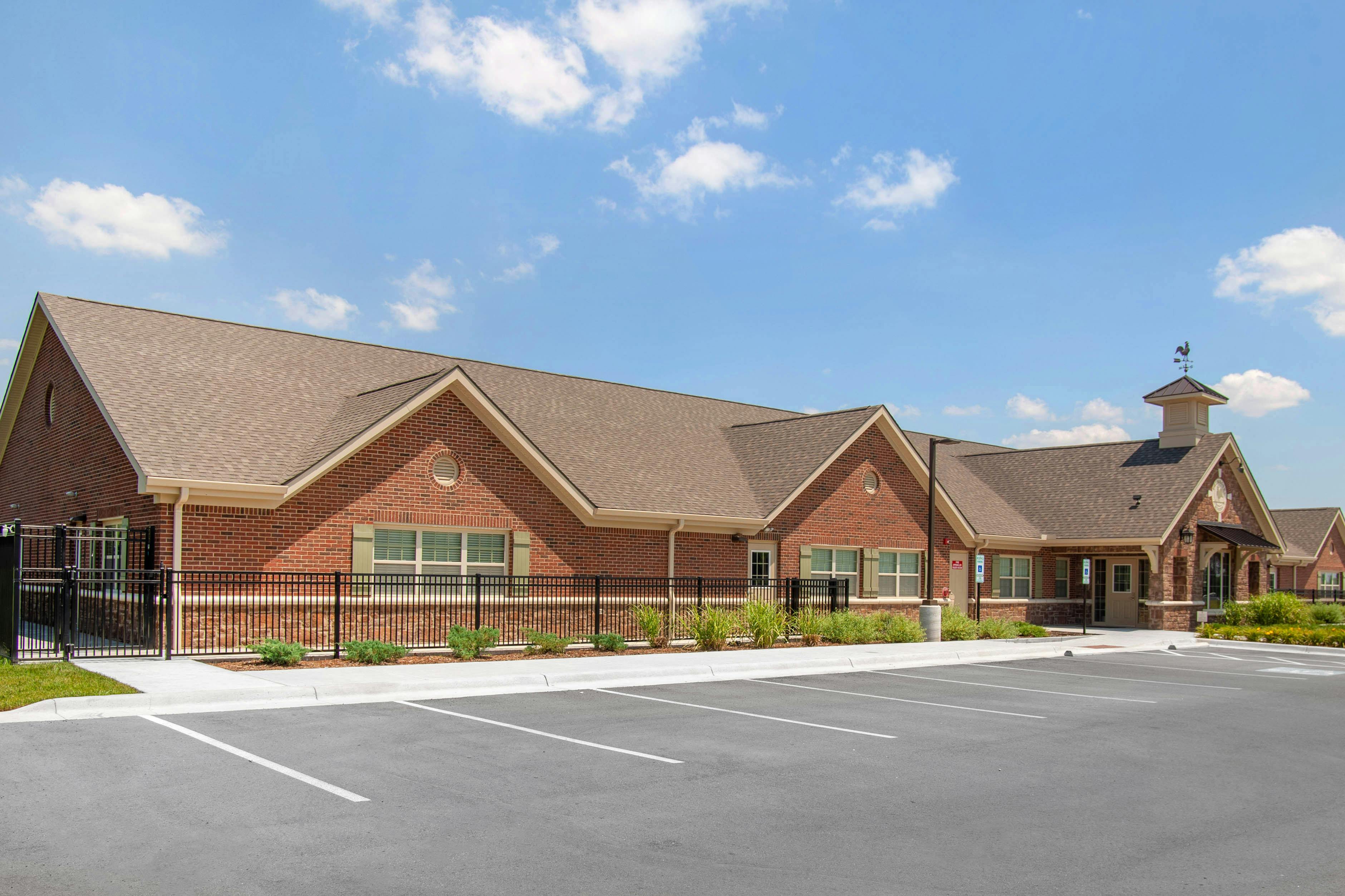 Brick building with a gray roof, small cupola with a weathervane, and a parking lot