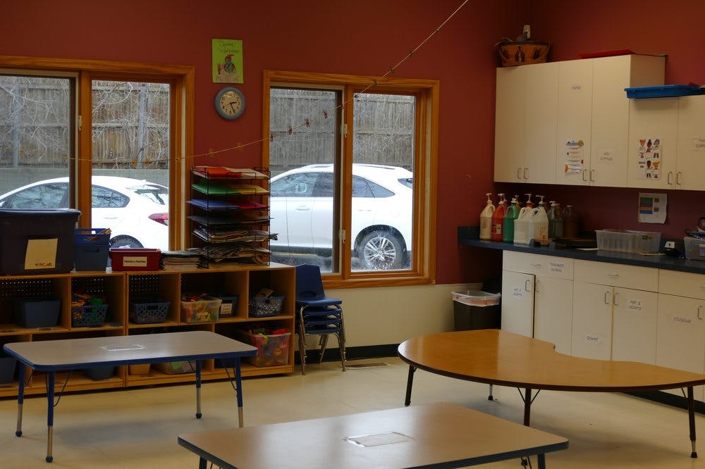 Classroom with tables, storage shelves, and windows looking out to cars