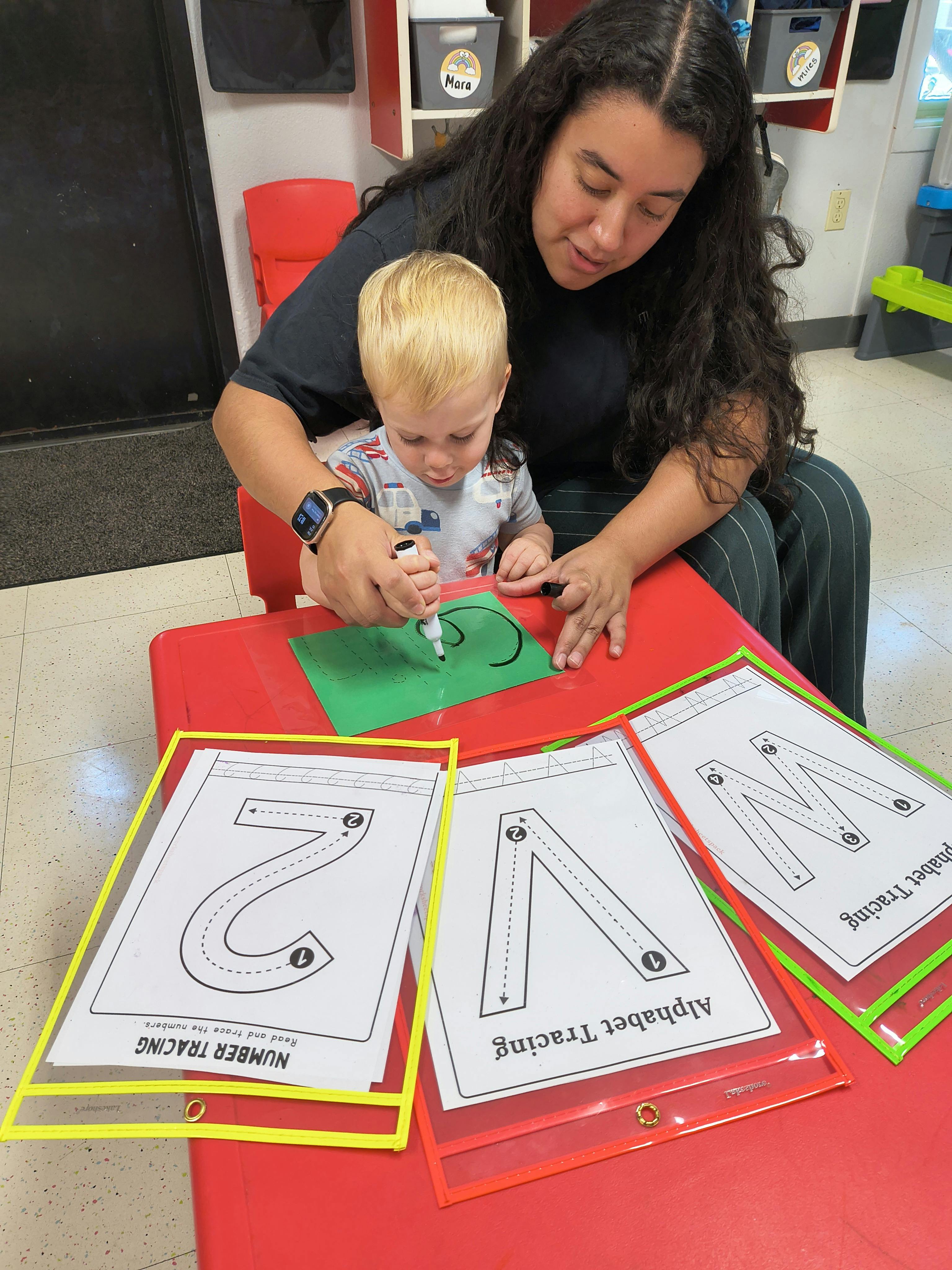 Adult helping a child practice writing on a worksheet at a table