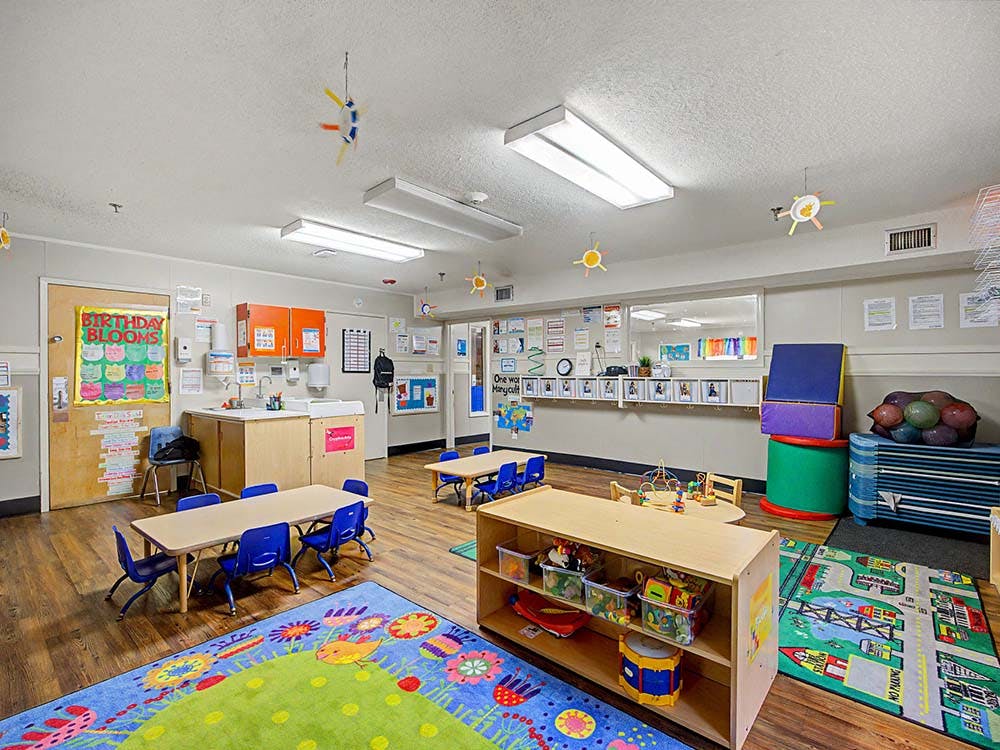 Classroom with small tables and chairs, a colorful rug, and a sink area