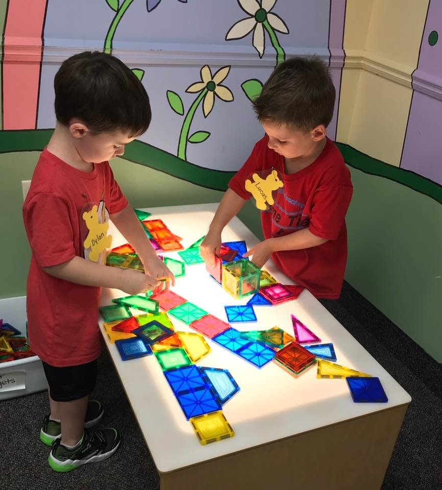 Two children playing with colorful translucent blocks on a light table