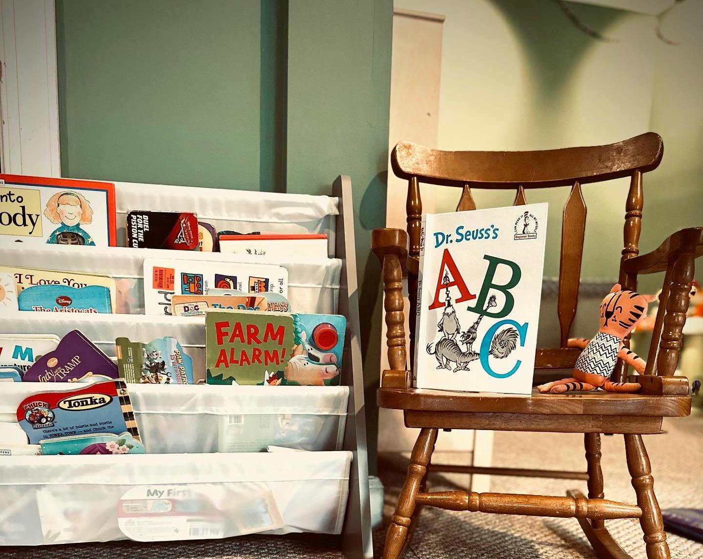 Children's books on a bookshelf next to a wooden chair with a book