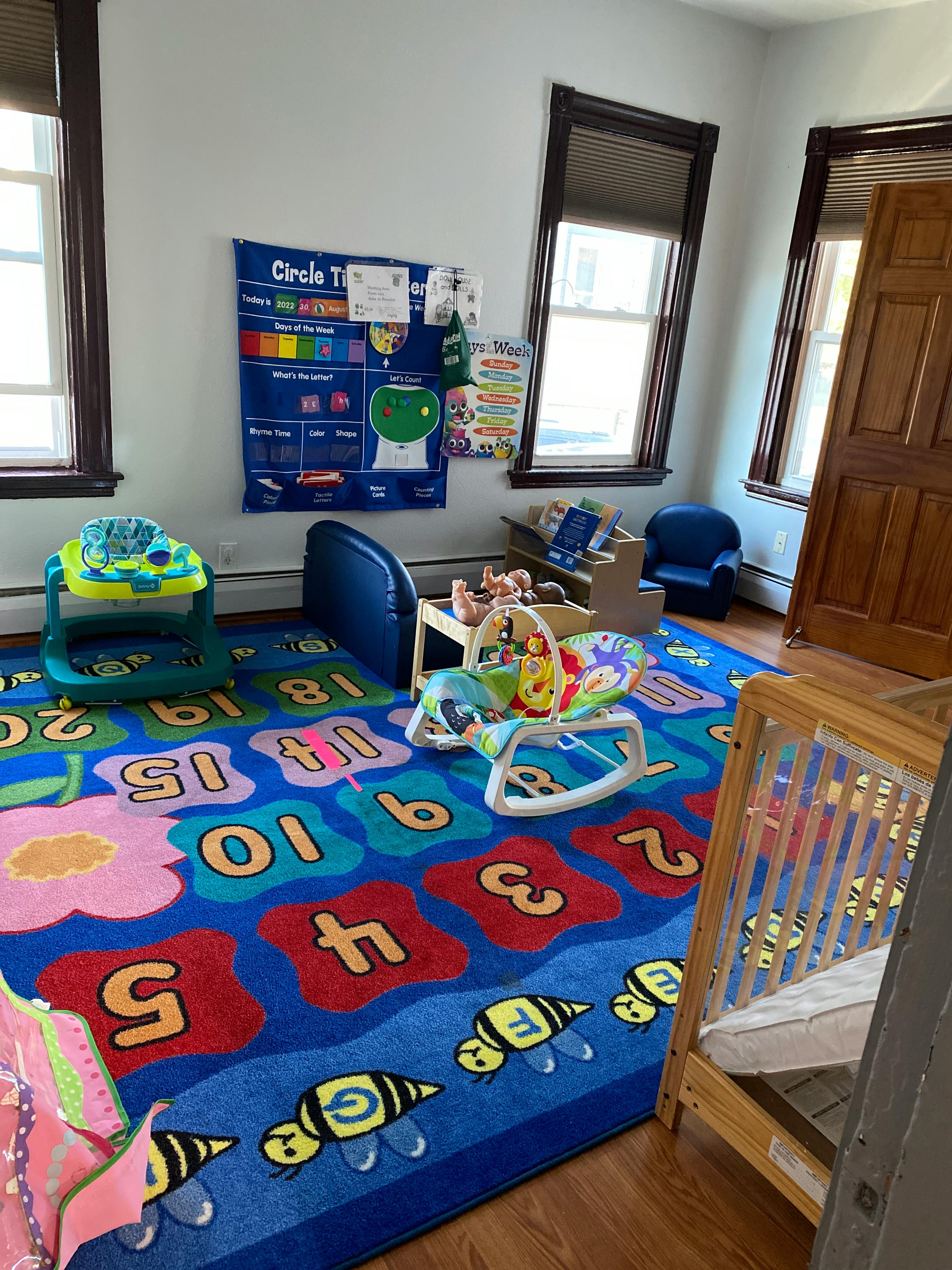 Playroom with a colorful rug, baby walker, bouncer, and crib